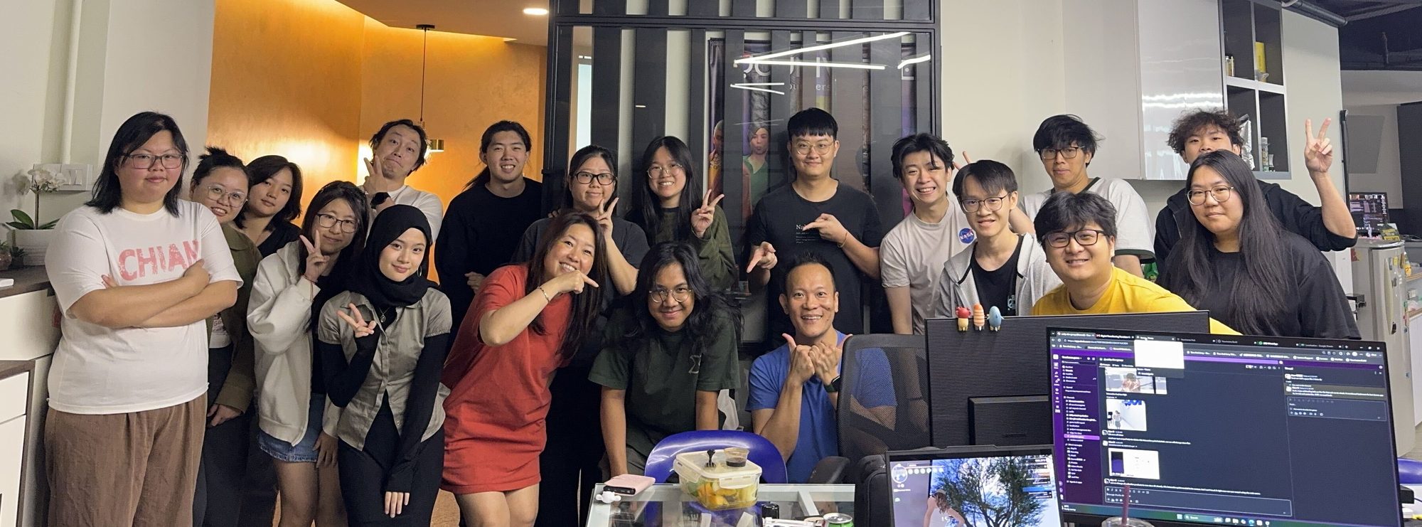 The Youniverse Games team in the office, posing with peace signs, pointing fingers and thumbs up